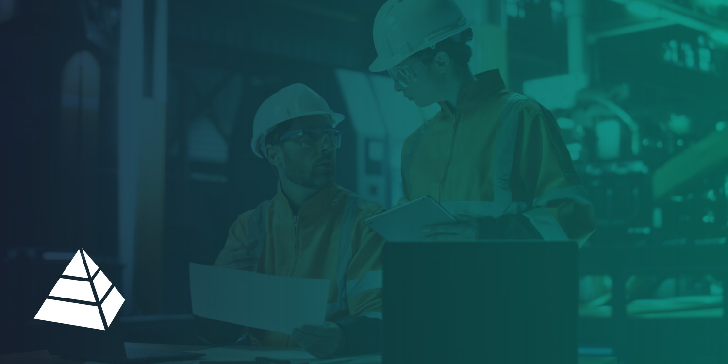 Two industrial workers in PPE reviewing procedure documentation on a worksite